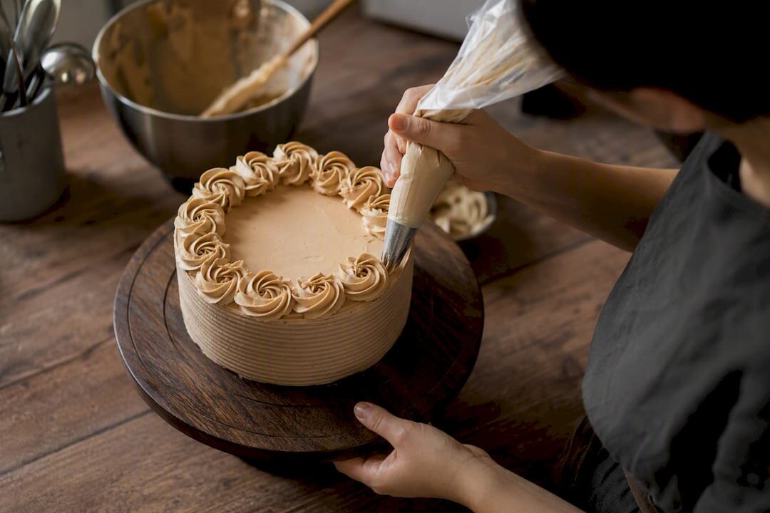 Manos decorando rosetas en una tarta sobre una plataforma giratoria