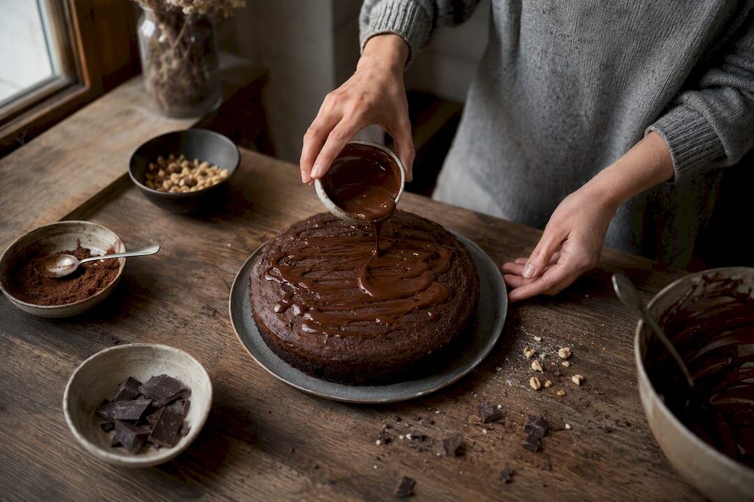 Manos dando los últimos toques a una tarta de chocolate con cacao en polvo